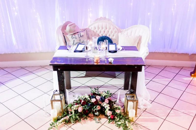 The sweetheart table and a tufted settee set on the tiled dance floor with florals, lanterns and candles along the base