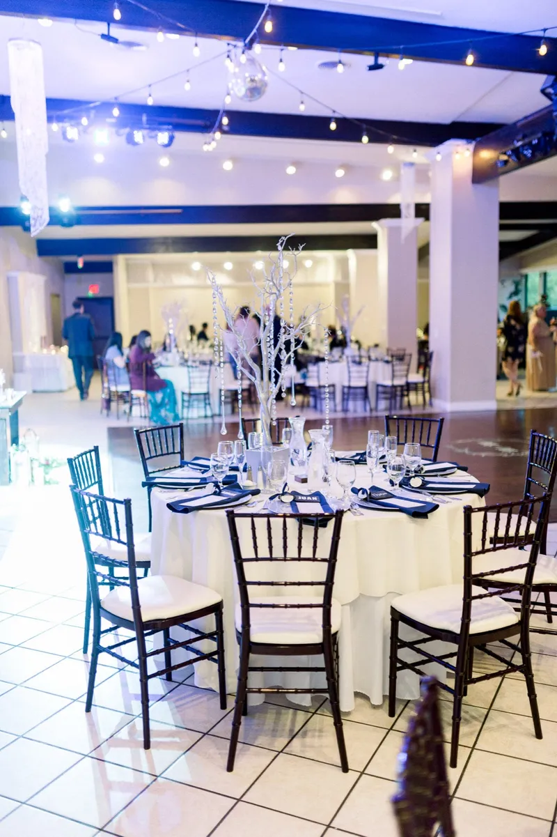 The reception hall full of guests at round tables with string lights overhead and a disco ball hanging over the dance floor