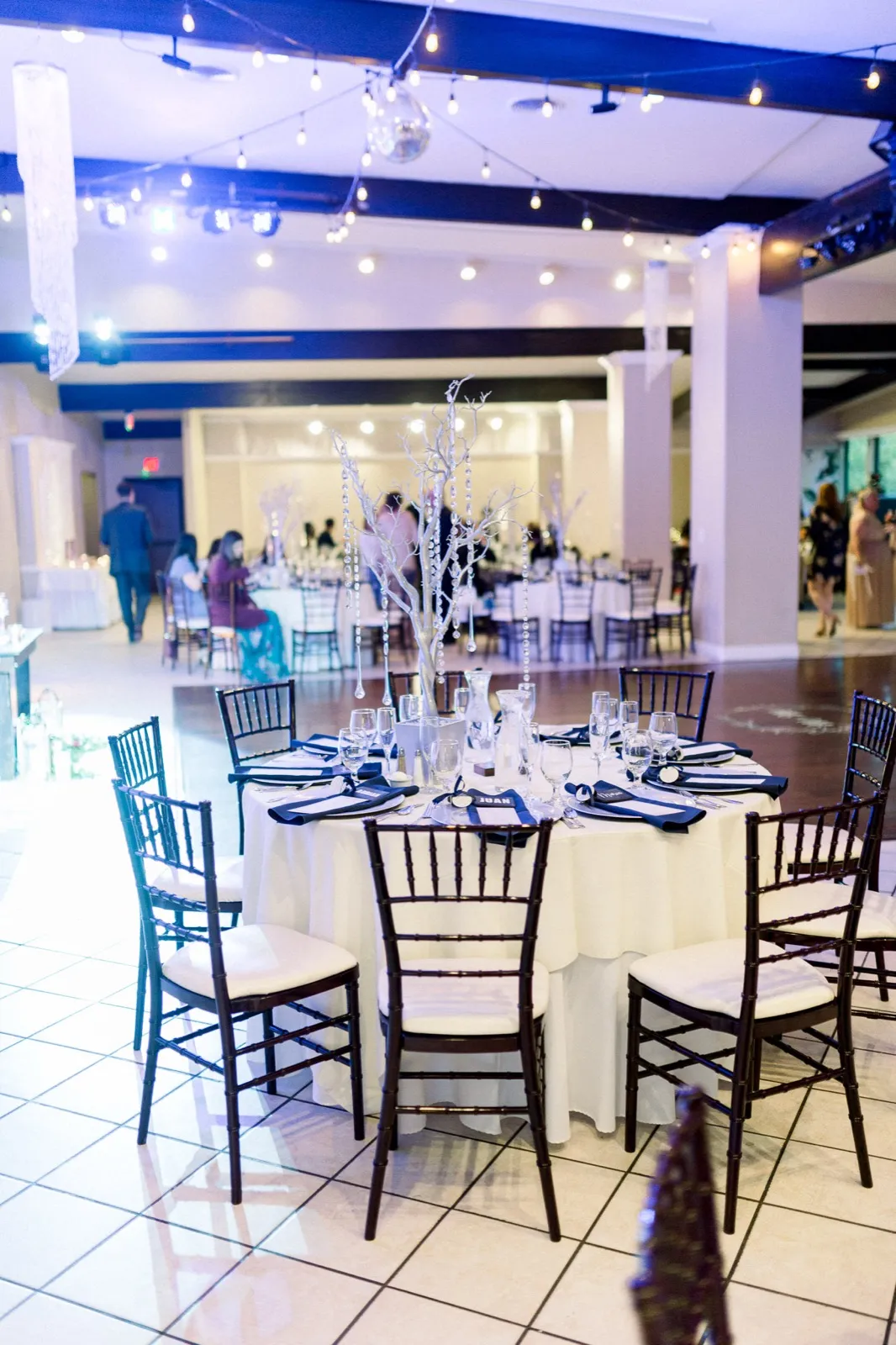 Guests at round tables in an indoor reception hall lit by string lights and a disco ball over the dance floor