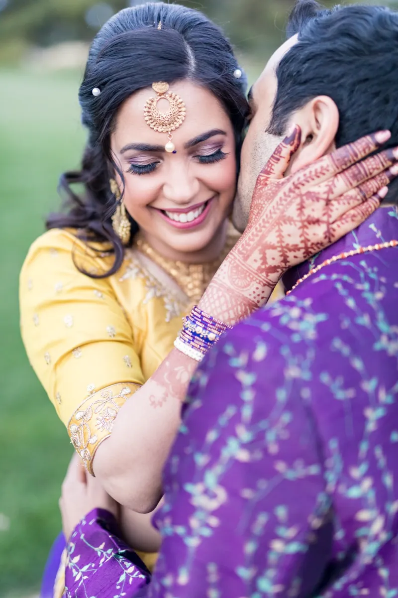 Close portrait of the groom kissing the bride's cheek while her henna covered hand rests at his neck