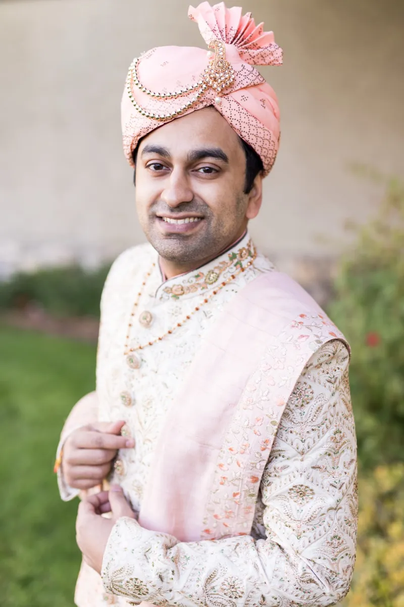 Groom on the lawn in a cream sherwani and a blush turban, one hand holding his stole