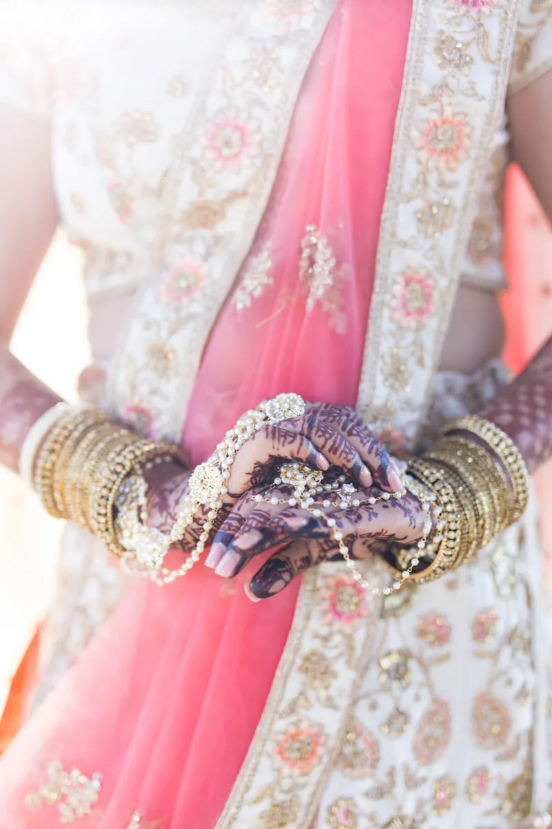 Close view of the bride's henna covered hands and stacked gold bangles held in front of her lehenga