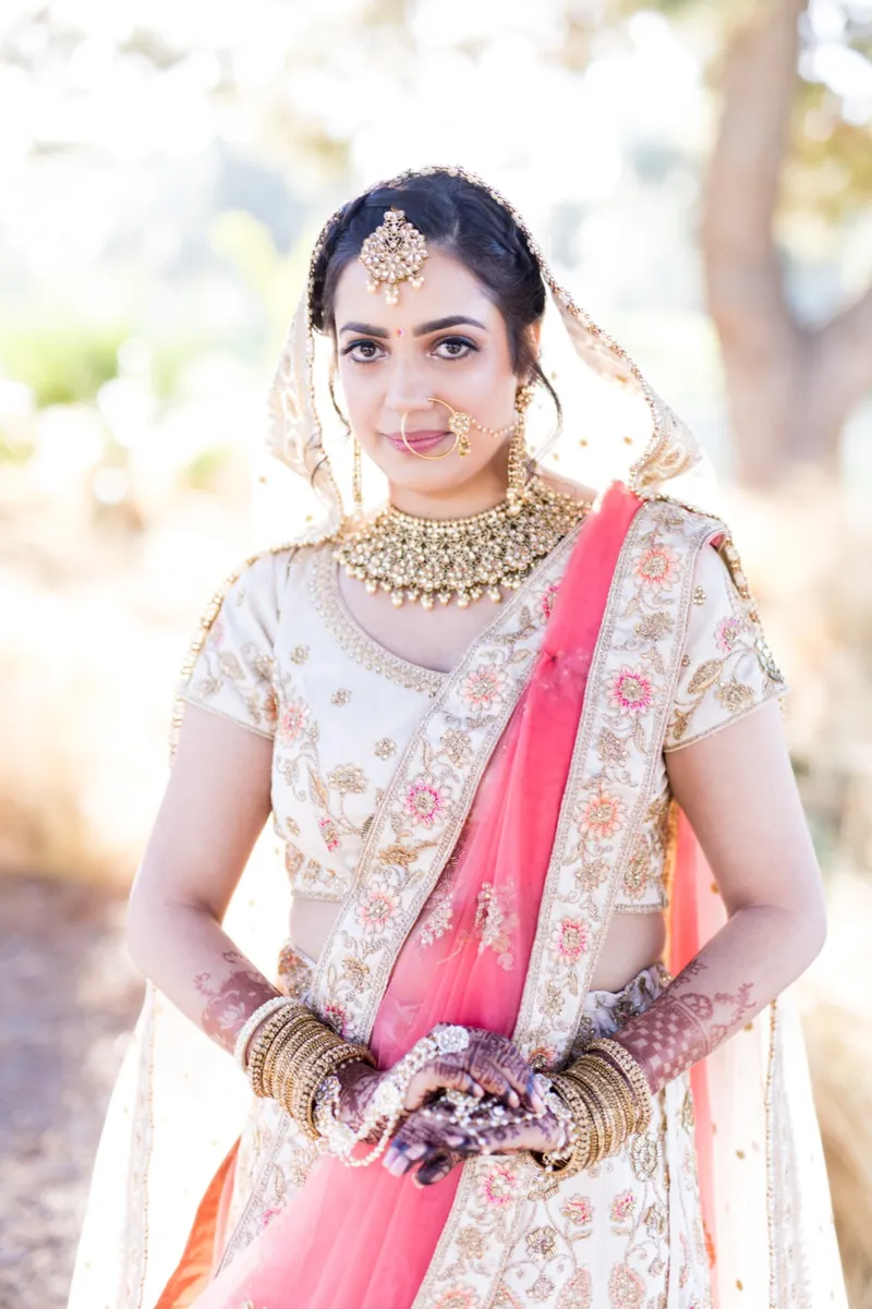 Bride looking straight to camera in her dupatta and gold bridal jewelry, the course soft behind her