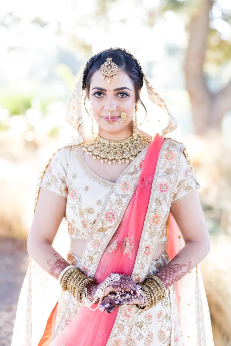 Bride in a pink and cream lehenga with gold jewelry at an Indian wedding