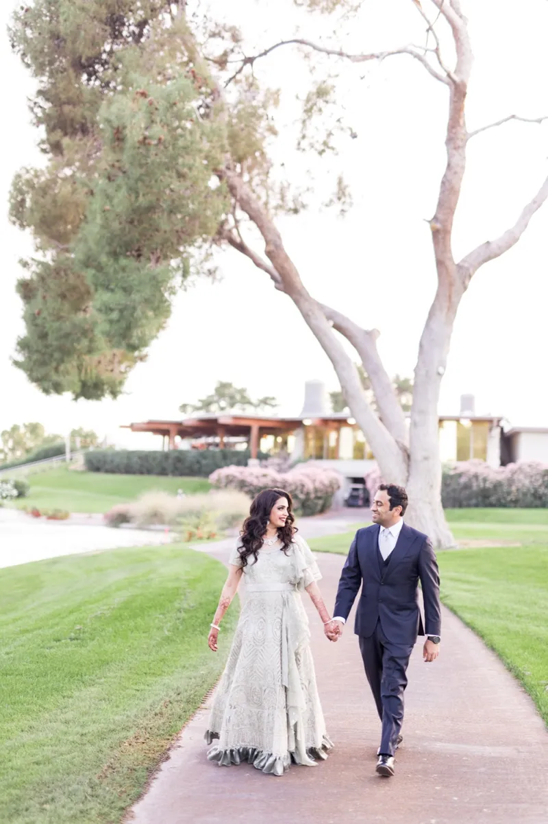 Bride in a pale embroidered reception gown walking the path with her groom, who has changed into a navy suit