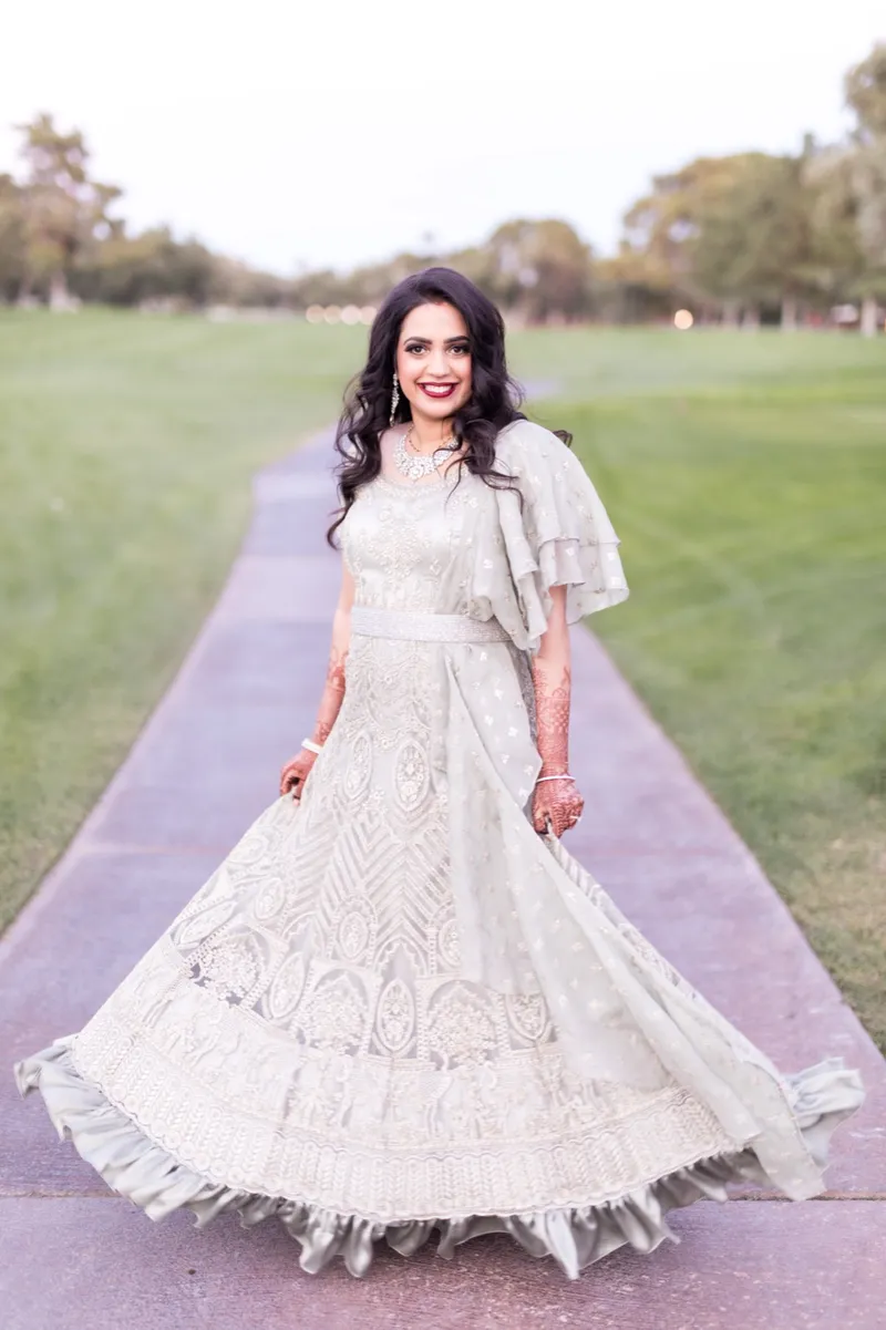 Bride swinging the skirt of her embroidered reception gown out wide on the path beside the grass
