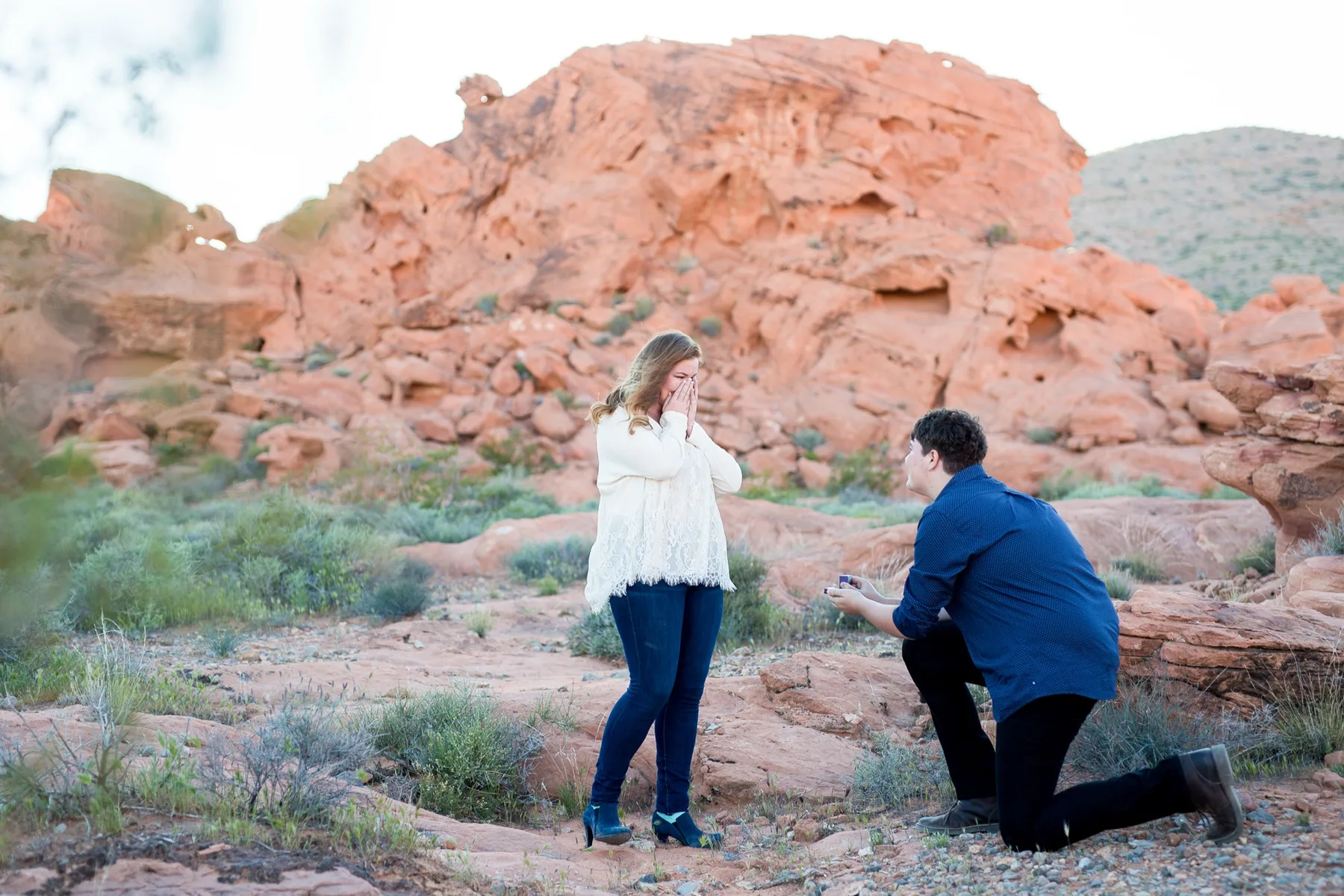 A man kneeling with the ring box open as his surprised partner covers her face at Valley of Fire