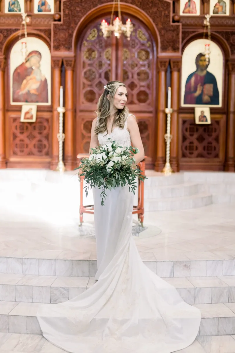 Bride standing alone on the white marble steps with her train spread behind her, the carved wooden icon screen filling the frame at her back