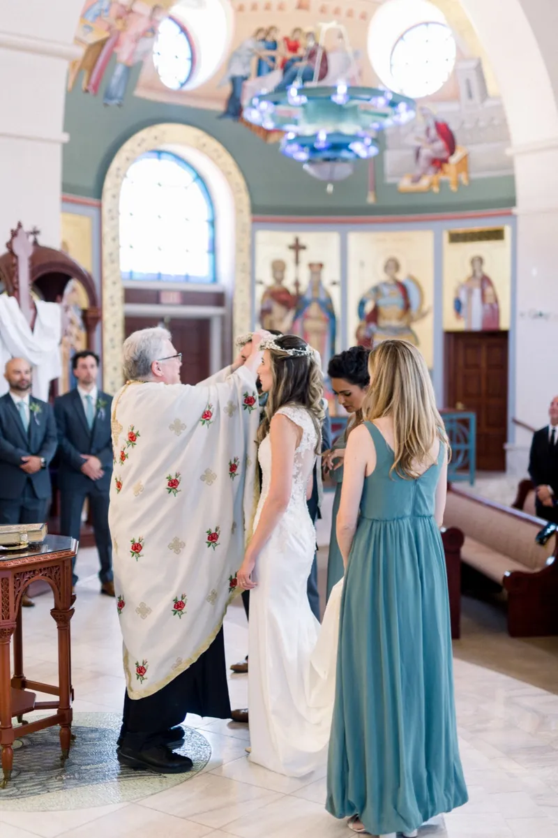 The crowns passing back over the couple's heads, seen from behind the bride with the arched stained glass windows above them