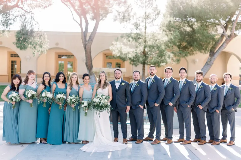 The whole wedding party lined up outside the church, bridesmaids in teal and sage on one side, groomsmen in slate suits on the other, the couple in the middle