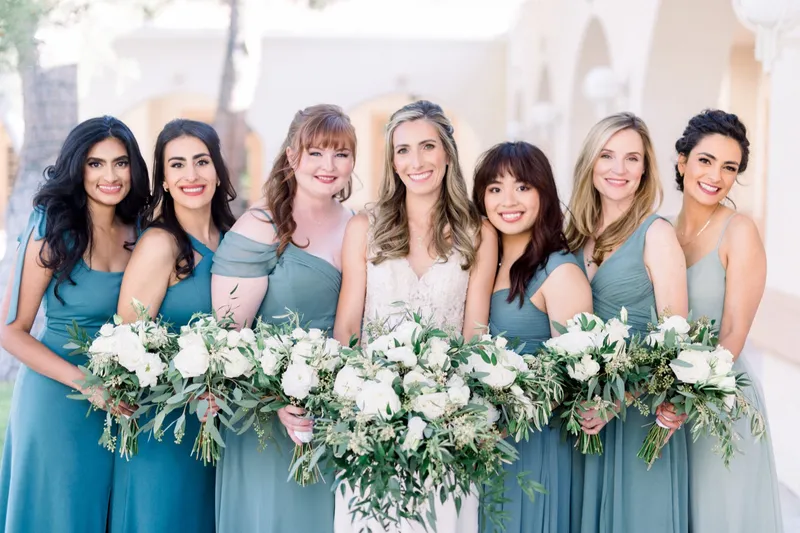 Bride and her bridesmaids pressed shoulder to shoulder with their white and olive bouquets held out in a row in front of them