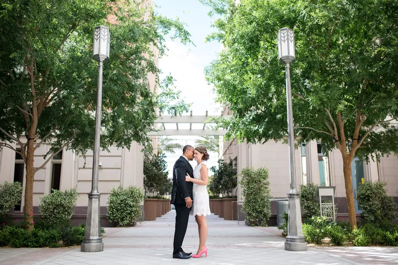 Couple standing forehead to forehead in the middle of a leafy courtyard, framed by two matching art deco lampposts
