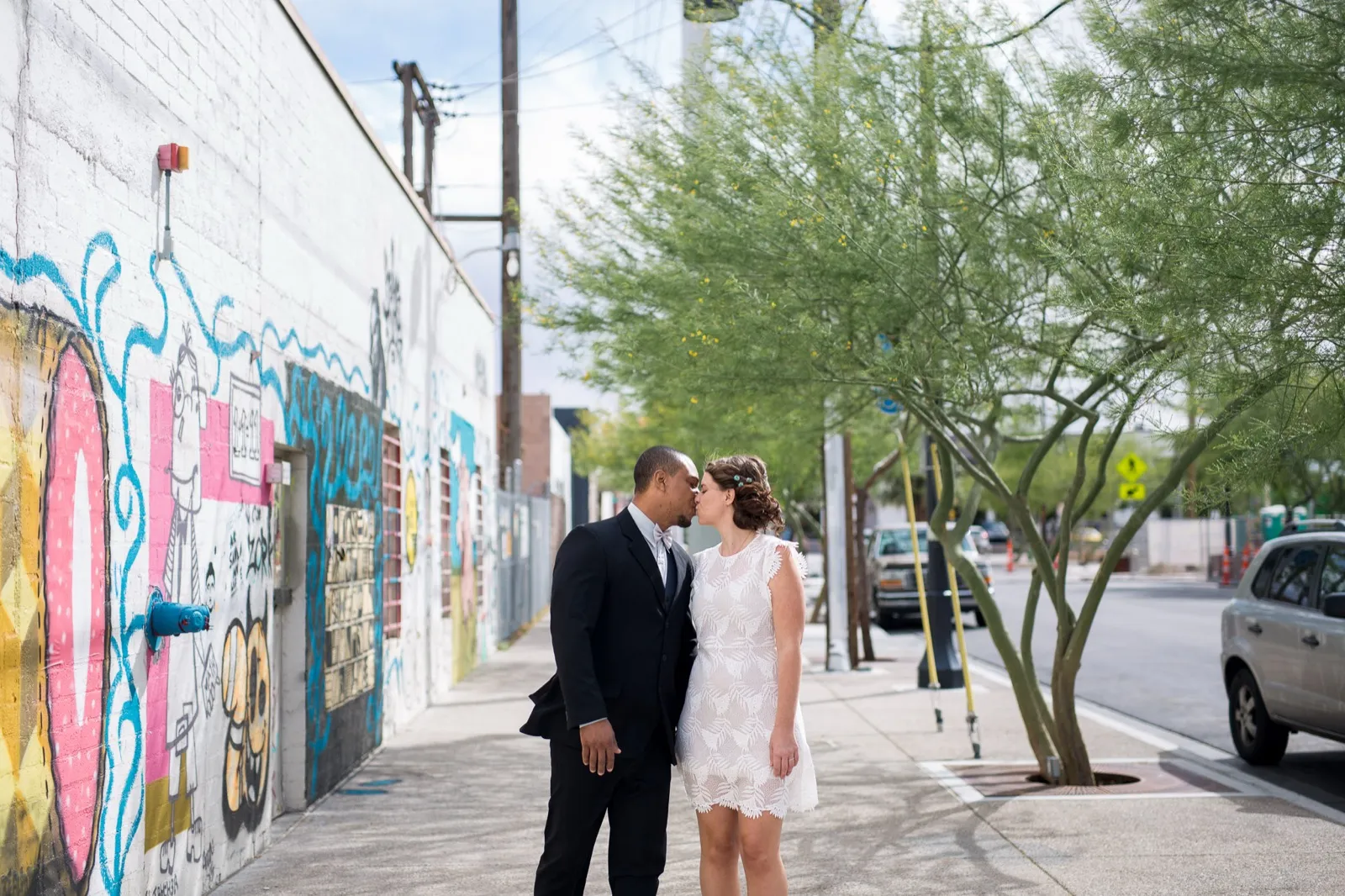 A couple kisses on a sidewalk beside a colorful mural wall in the Arts District in downtown Las Vegas