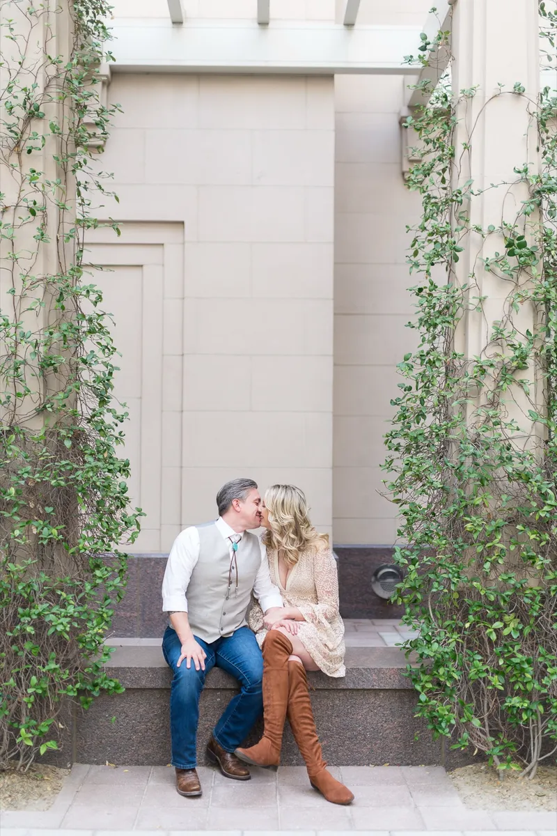 Couple in their forties kissing on the stone ledge between two columns of green vines