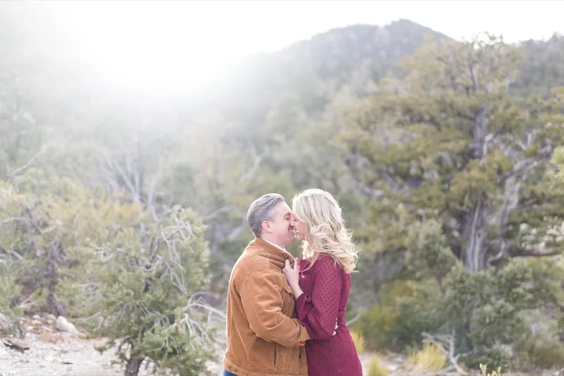 Man kissing his fiancee with the sun flaring over the ridge behind them