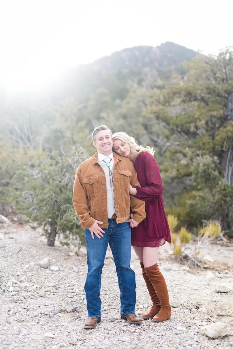 Couple standing together on the gravel with junipers and a hazy peak behind them