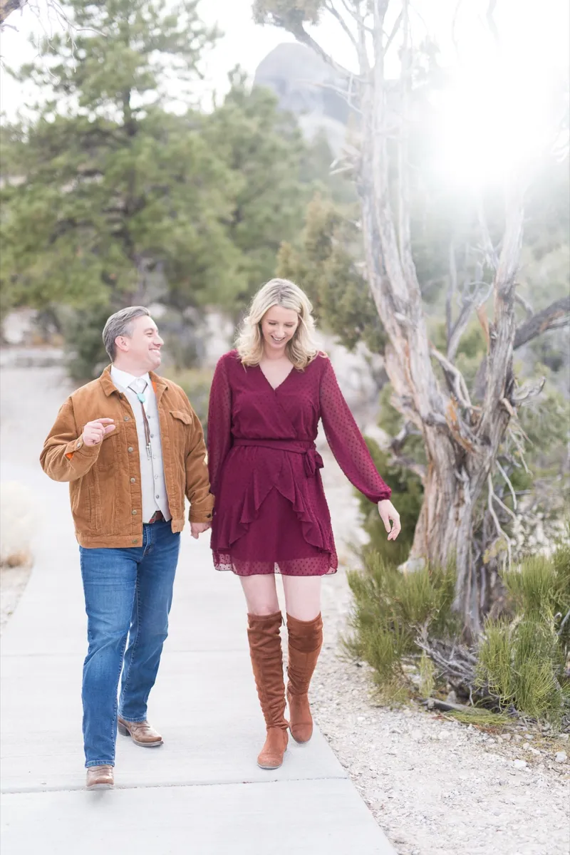 Couple walking up a paved path toward the camera, her in a burgundy dress and tall brown boots