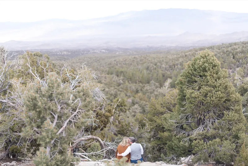 Wide view of the couple sitting small on a fallen log at the edge of an overlook above the valley