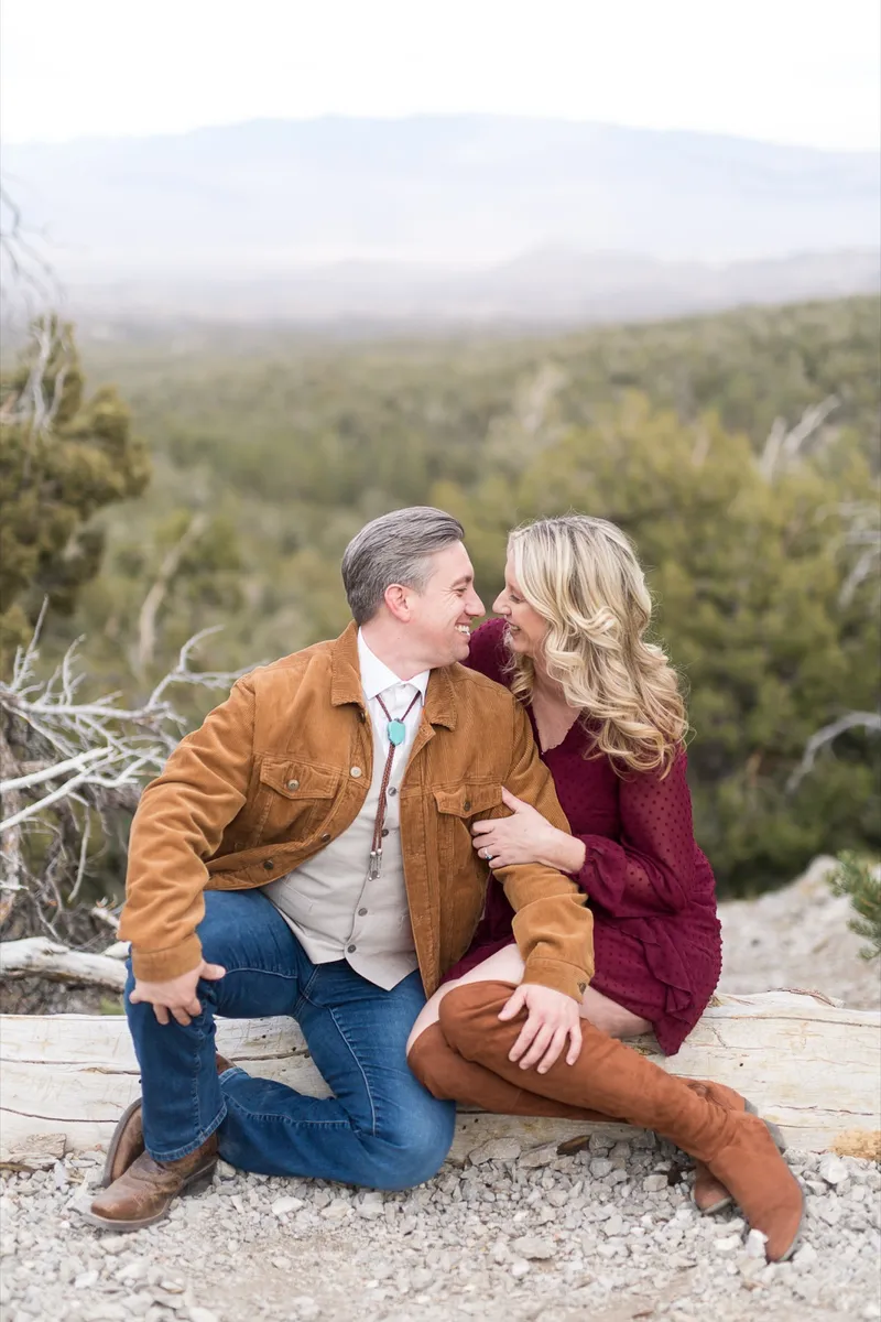 Man kneeling beside a fallen log with his fiancee leaning into him, both of them laughing