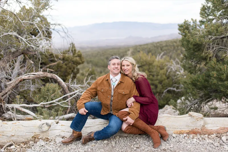 Couple sitting on a fallen log facing the camera with the valley spread out behind them