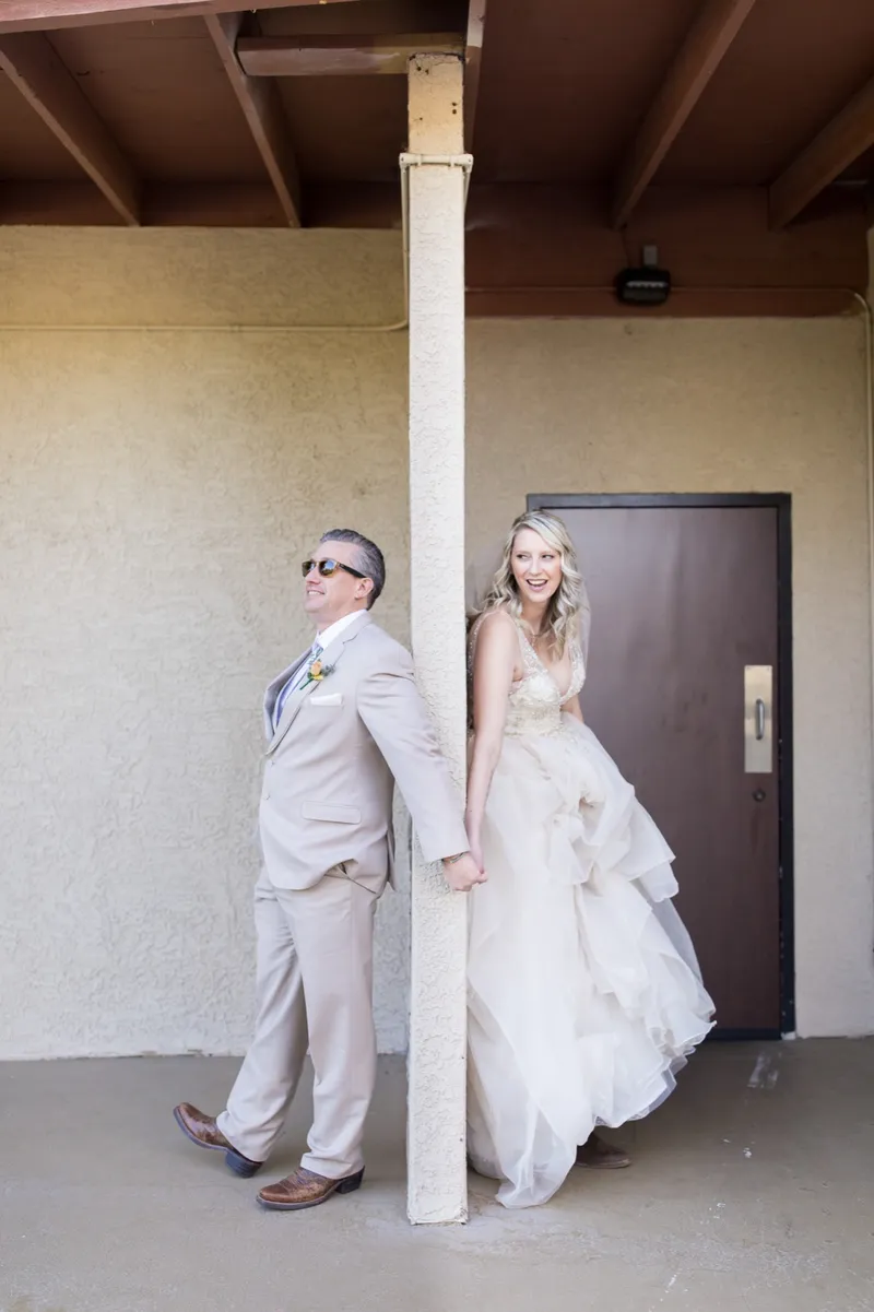 A bride and groom holding hands around opposite sides of a post outside the venue building before seeing each other
