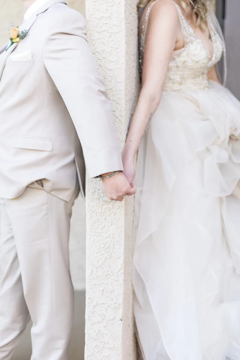 Close crop of the couple's joined hands around the post, her ruffled skirt and his tan suit on either side