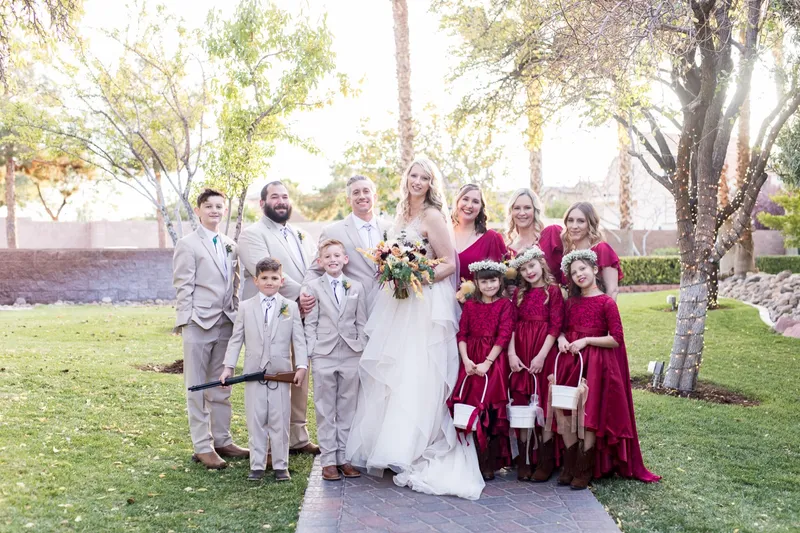 The full wedding party gathered on the lawn, the men in tan suits and the women and girls in deep red