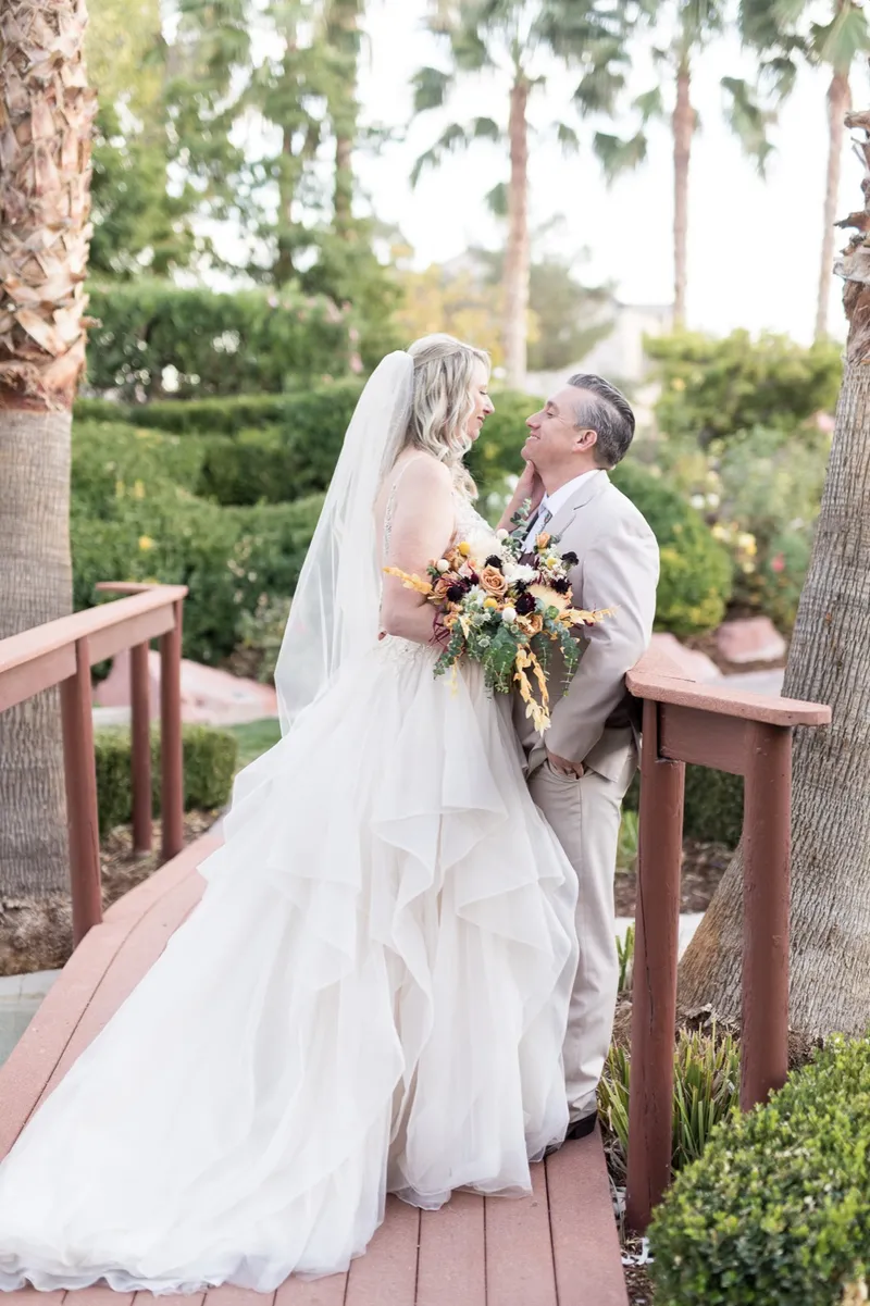 The bride leaning back laughing with the groom on the wooden footbridge, palms rising behind them