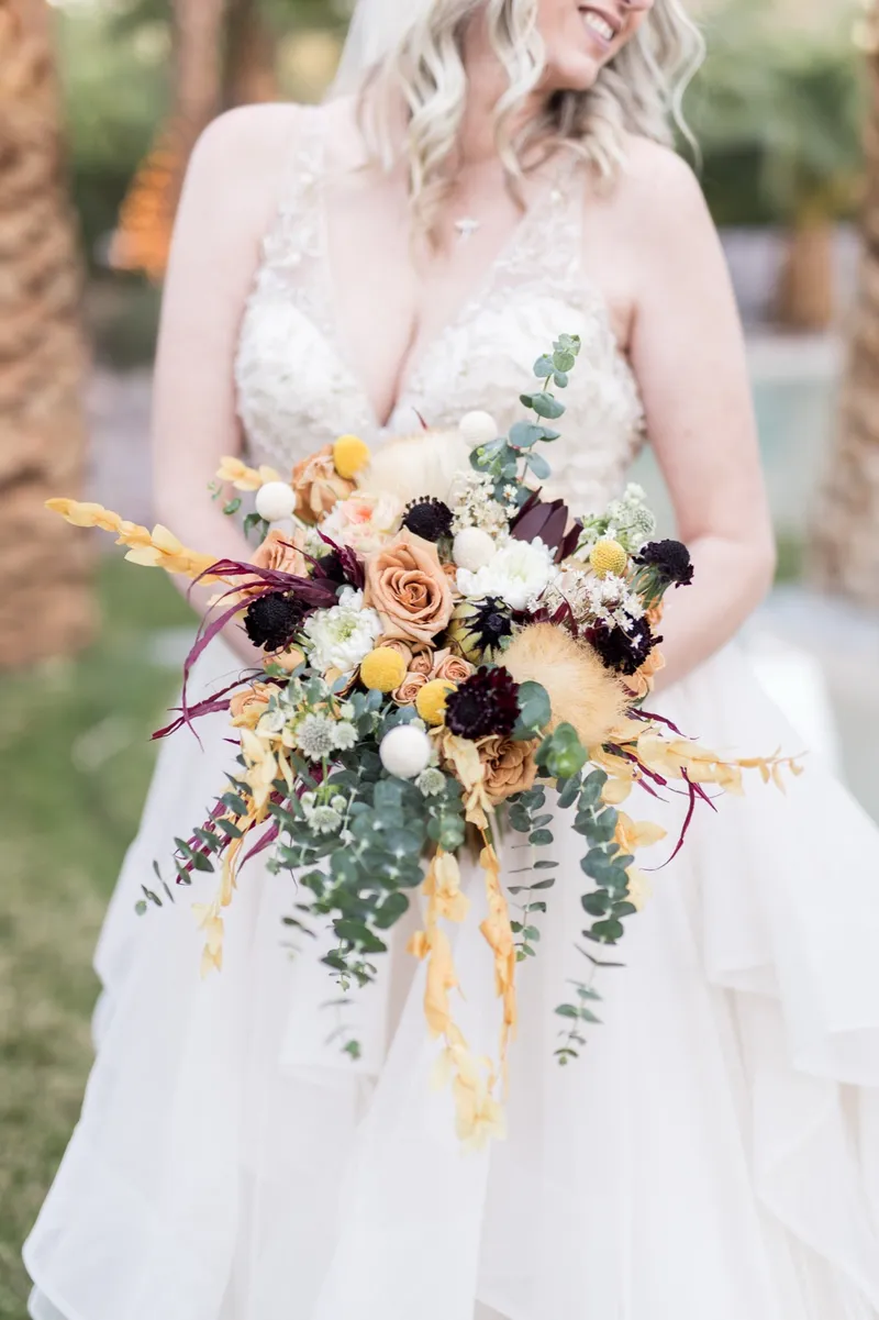 Close view of the bride's hands holding a bouquet of roses, eucalyptus and dried blooms against her ruffled gown