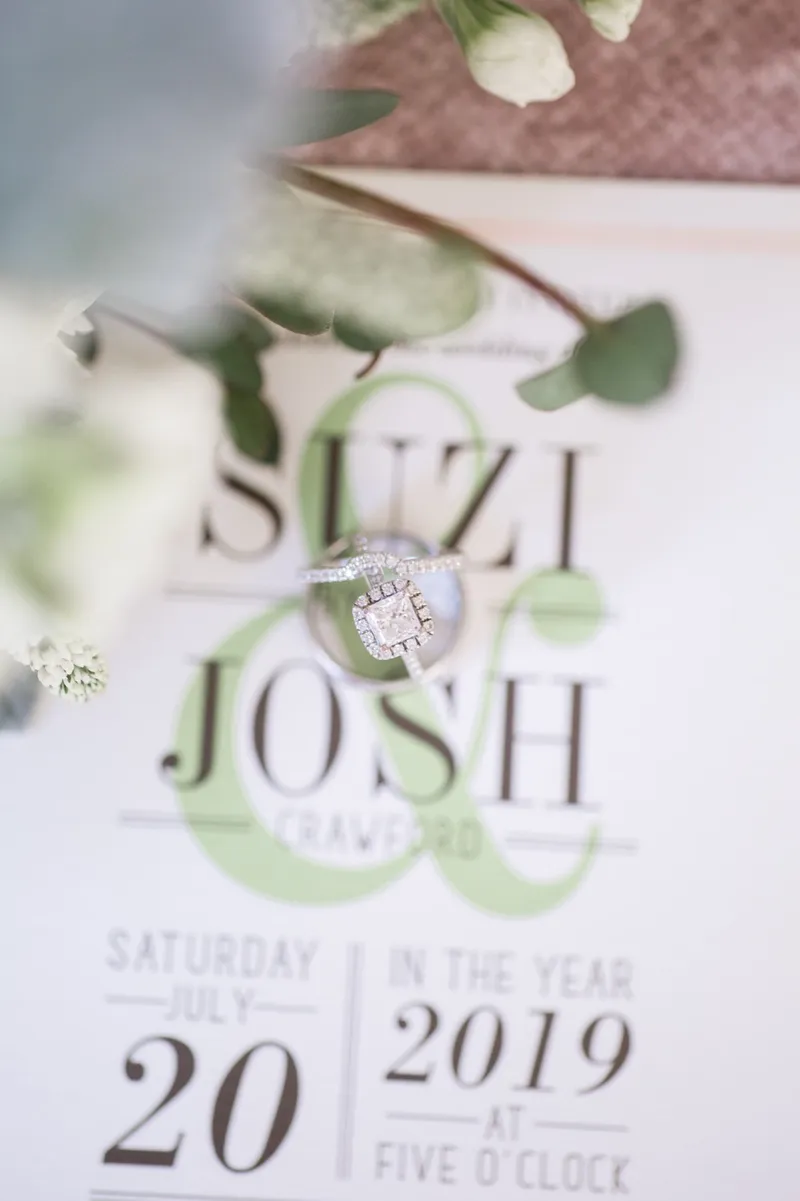 The engagement ring resting on the couple's printed invitation with white blooms and eucalyptus leaves above it
