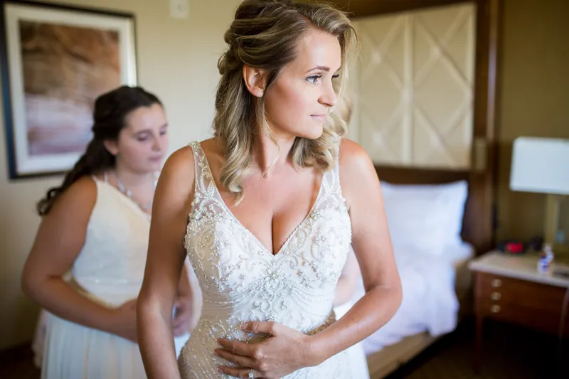 Bride standing in her beaded gown while someone behind her fastens the back