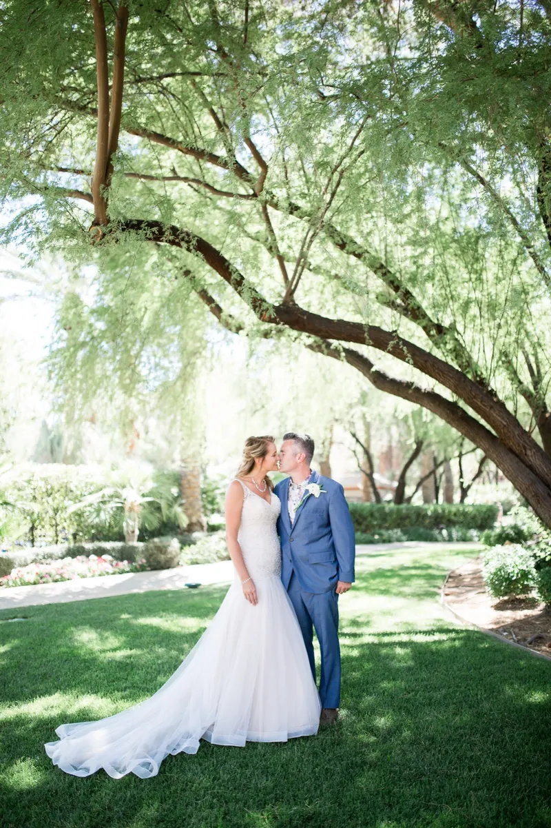 Bride and groom kissing on the grass under the low spreading branches of a shade tree