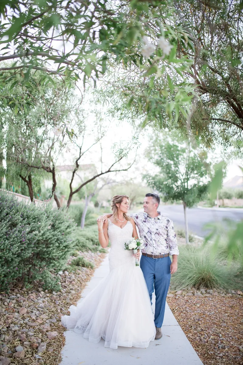 Couple walking the path together, the groom in a floral shirt and blue trousers and the bride in a full tulle skirt