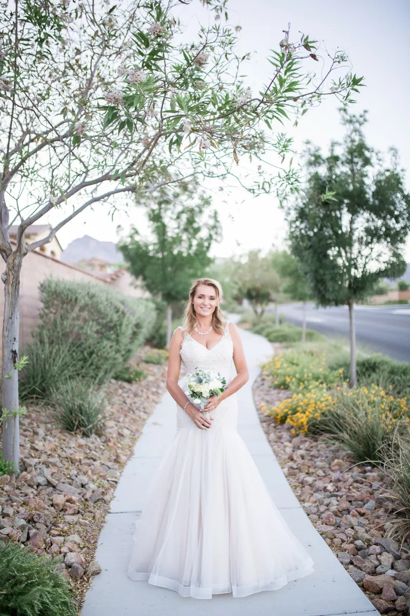 Bride standing alone on the walkway between clipped hedges holding her white bouquet
