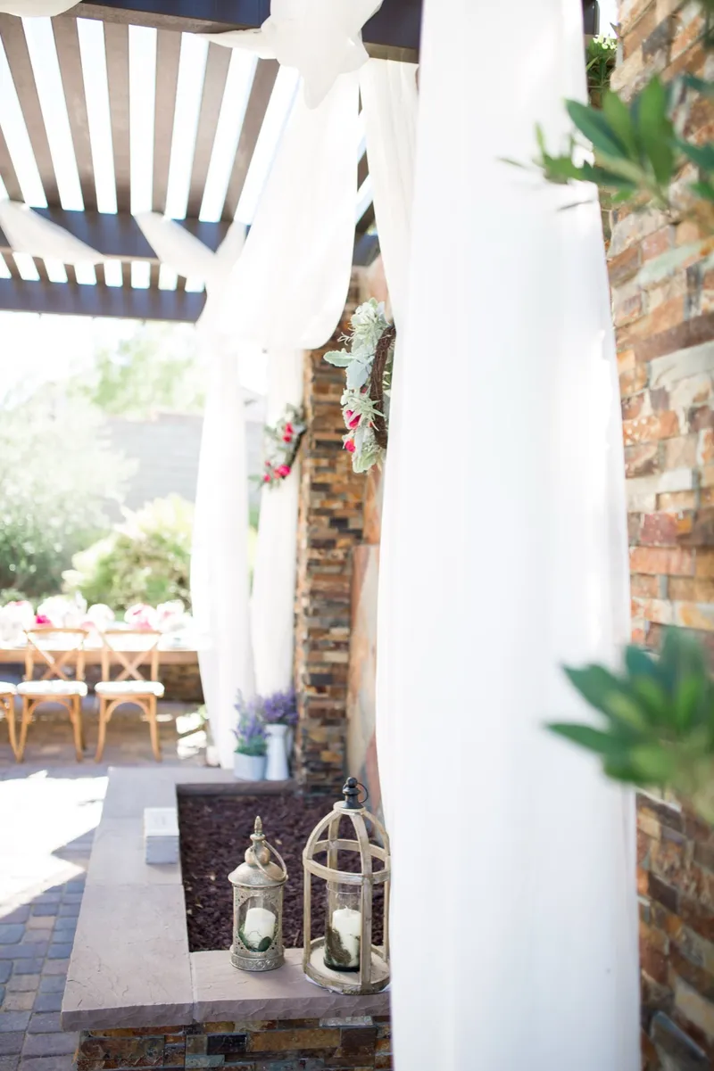 Close view of the draped pergola at the altar with hanging lanterns and florals against the tiled stone wall