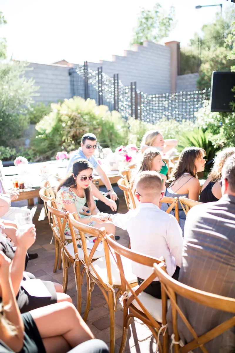 Guests seated in the wooden chairs under the pergola, chatting and waiting for the ceremony to start