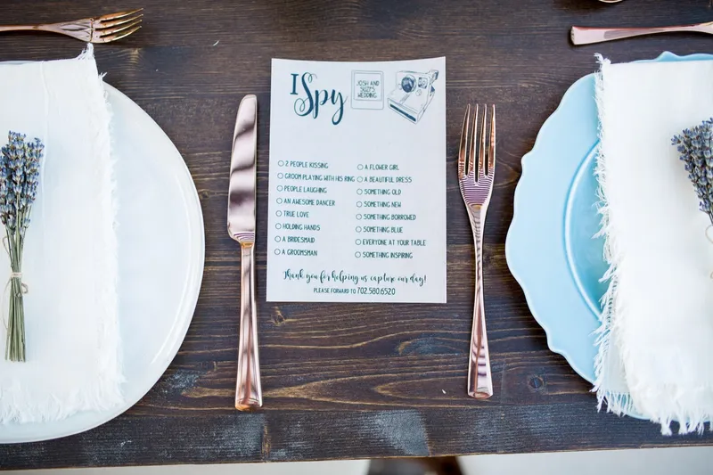 Place setting with an I Spy card, rose gold flatware, a sprig of lavender and a pale blue plate on the wood table