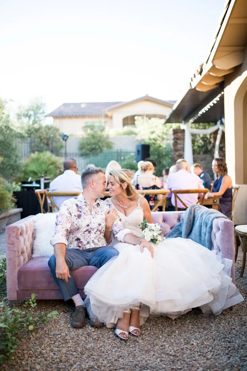 Couple sitting together on a pink velvet sofa at the edge of the backyard reception