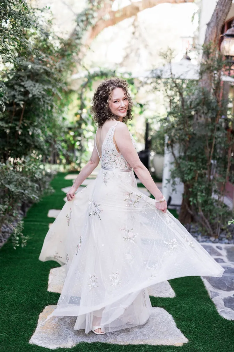Bride holding her embroidered tulle skirt out to both sides on the garden walkway with lanterns and greenery around her