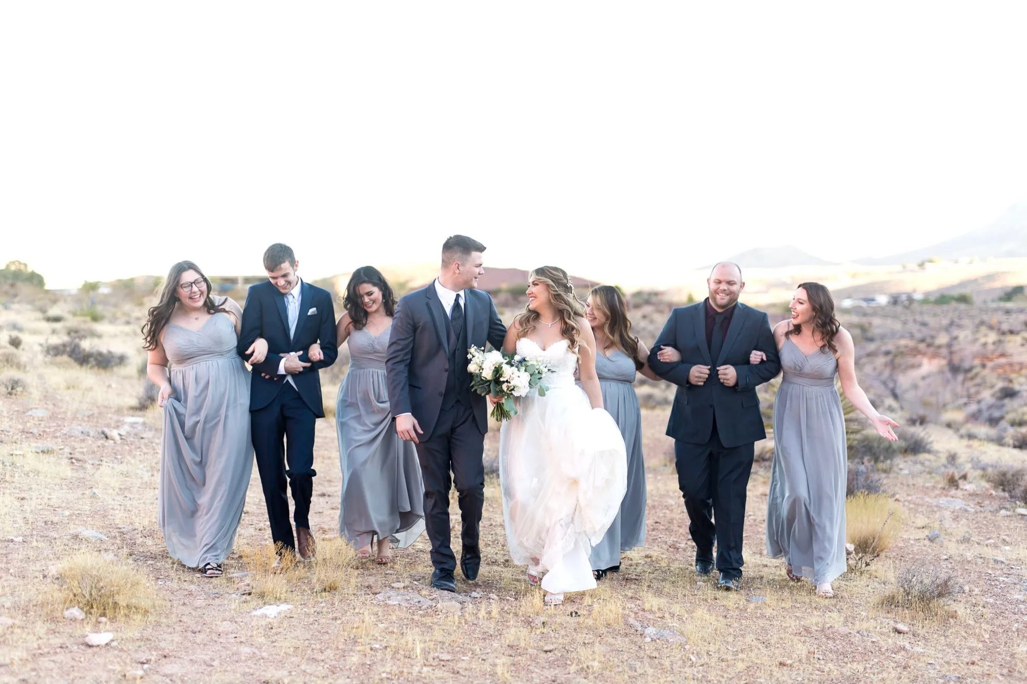 A bridal party walking arm in arm through golden desert grass in the soft evening light outside Las Vegas