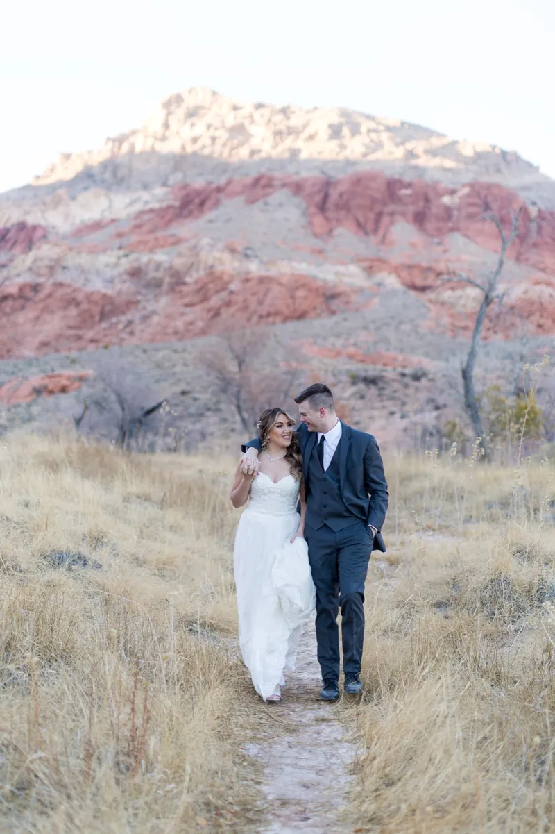 Bride and groom walking together through the dry grass toward the camera
