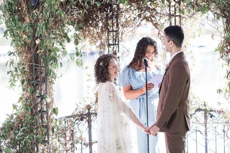 Couple holding hands at the altar while the officiant reads, the iron railing and the lake behind them