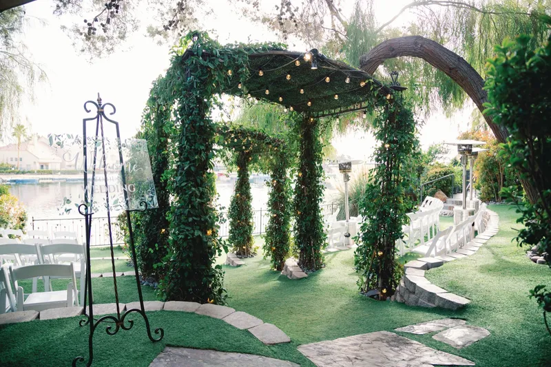 Wide view of the ceremony lawn with the row of leafy arches, white chairs set to one side and the lake and rooftops behind