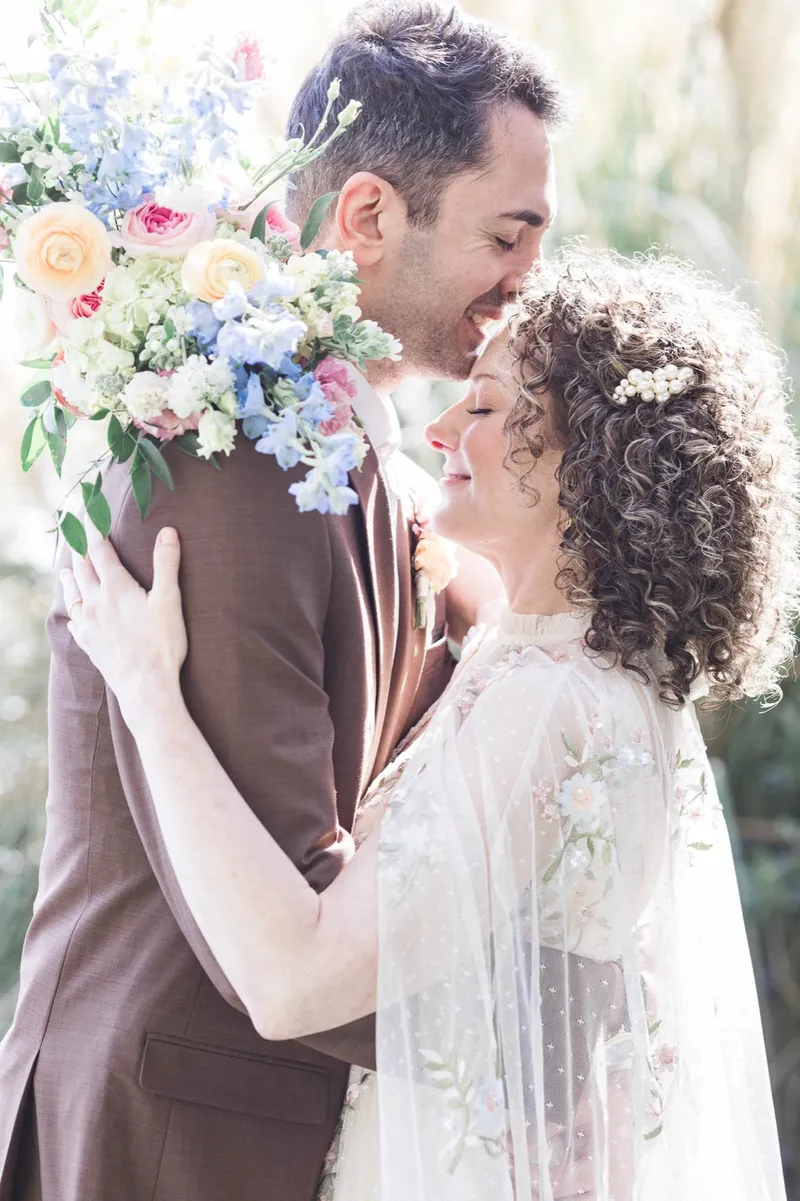 Couple laughing in each other's arms with the bouquet of blue delphinium and peach roses lifted beside them