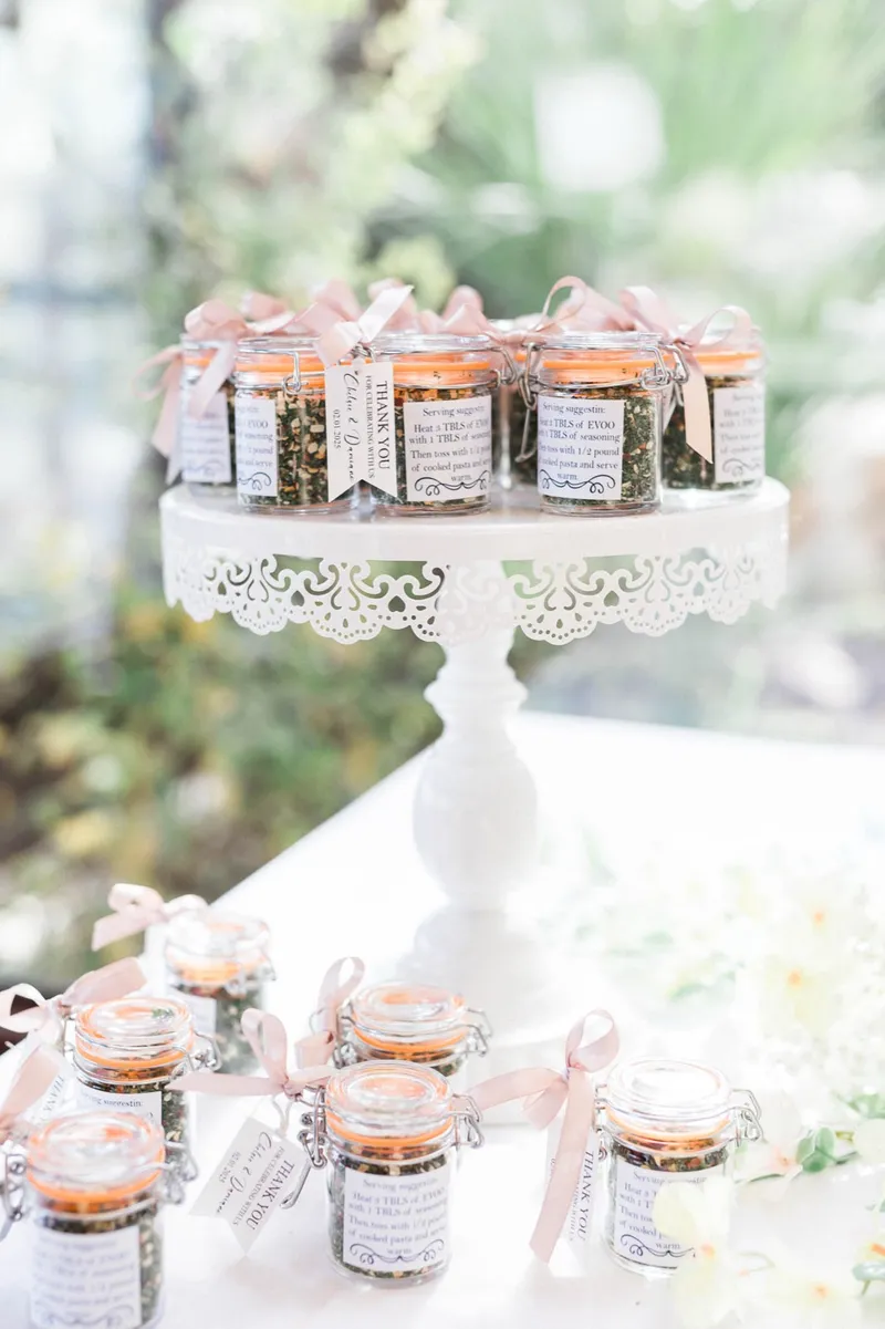 Small jars of loose tea tied with blush ribbon, arranged on and around a white lace cake stand
