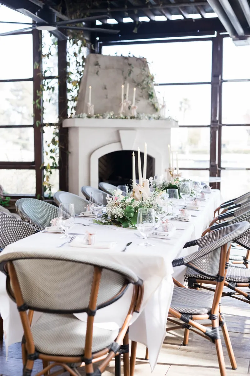 Reception table running past a stone fireplace hung with greenery, rattan bistro chairs pulled up on both sides