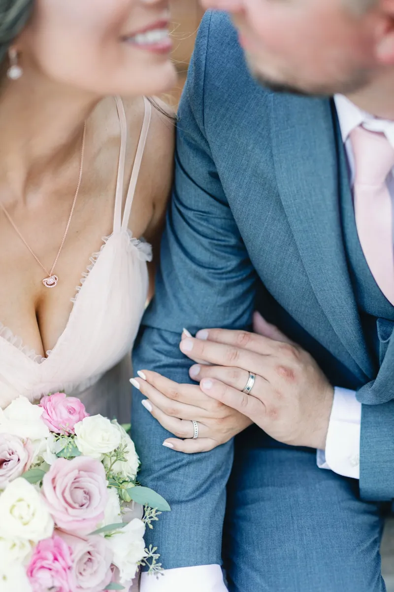 Close frame of the couple holding each other with her ring hand resting on his lapel and the bouquet below