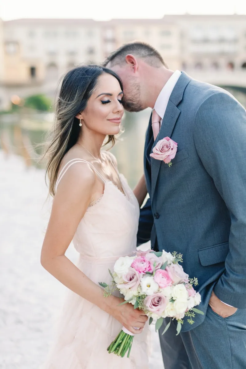 Groom kissing the top of the bride's head while she holds her bouquet against her chest