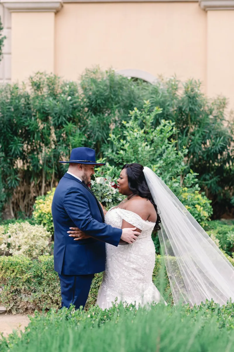 Bride and groom holding each other after the first look with her long veil trailing across the grass
