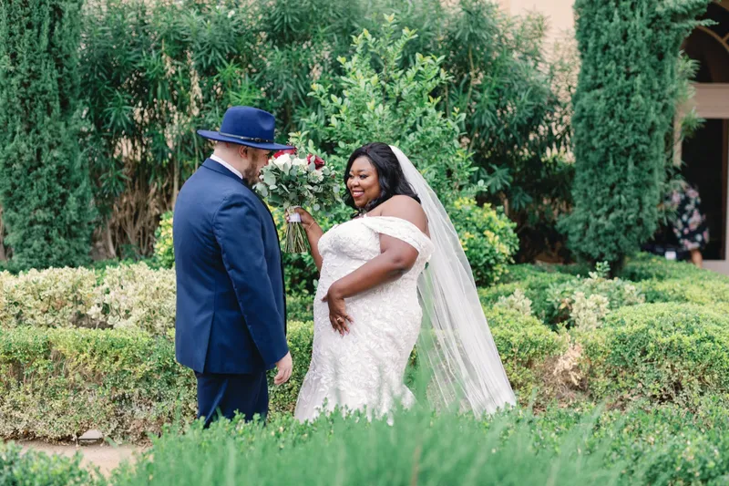 Groom leaning in to smell the bride's red and white bouquet while she laughs